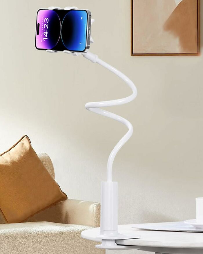 Flexible white phone holder mounted on a table holding a smartphone in a cozy living room setting, Amazon haul find.
