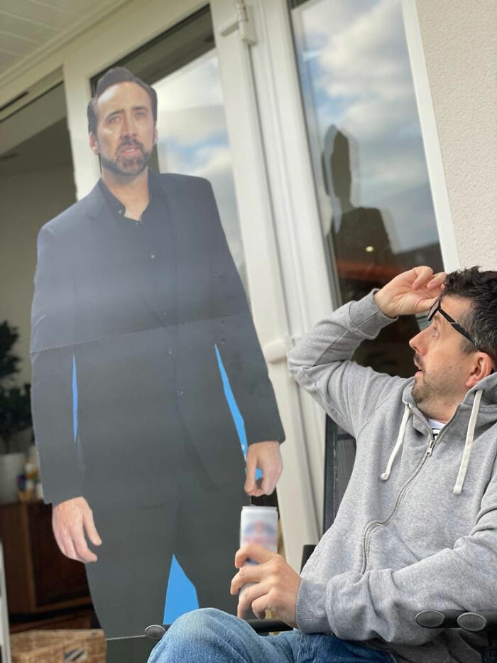 Man surprised by a life-sized cardboard cutout, sitting with a drink in hand, illustrating a weird encounter in someone's house.