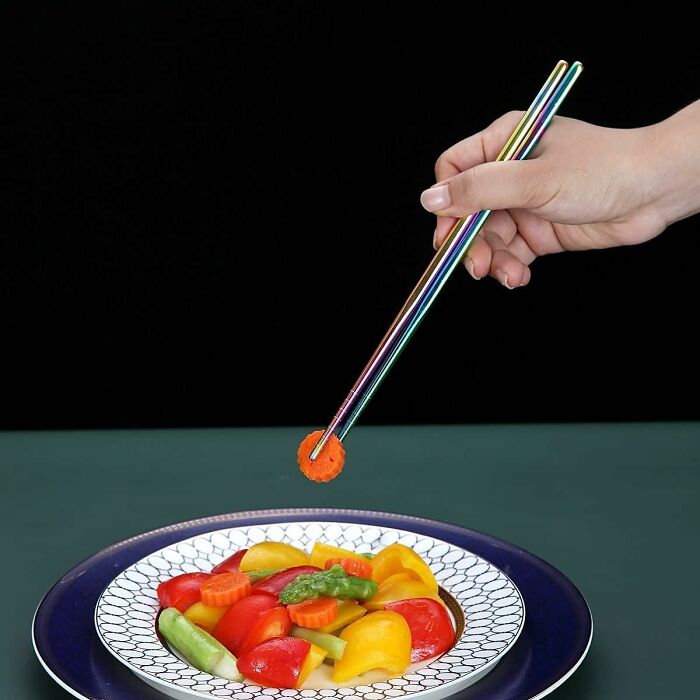 Hand using colorful chopsticks to pick a carrot from a vibrant vegetable dish, related to Amazon haul shopping.