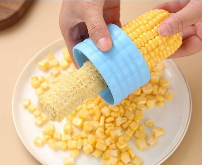 Hands using a blue corn s******r to remove kernels onto a plate, showcasing popular Amazon haul kitchen deals.