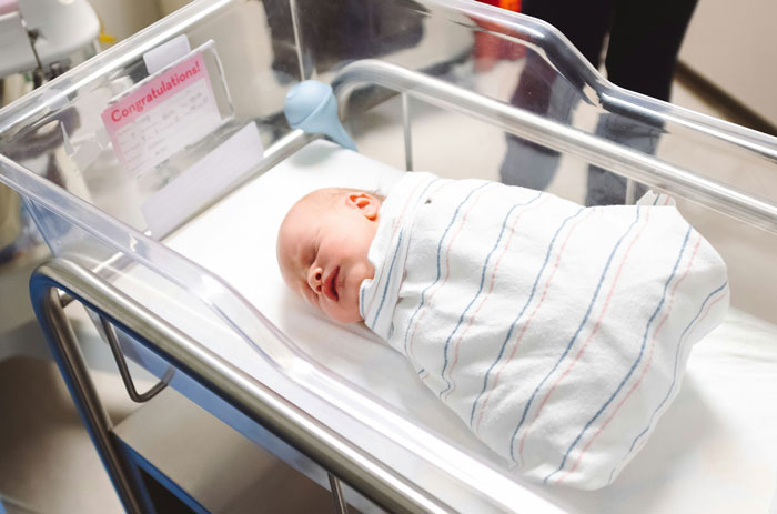 Newborn baby in hospital bassinet wrapped in a striped blanket, related to family DNA results discussion.