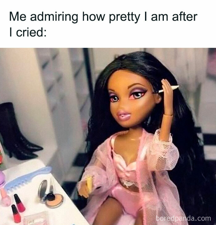 A doll smiling confidently at her reflection after crying, surrounded by makeup items on a dresser.