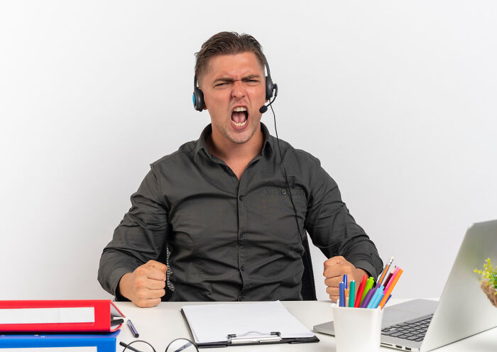 Man in headphones at a desk, visibly angry, embodying dramatic work tensions.