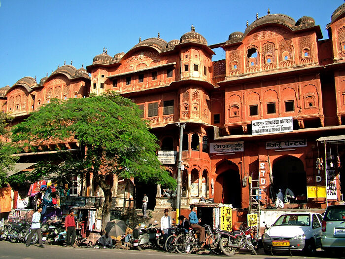 Colorful city street with vibrant architecture, lively market, and people passing by, resembling a real-life painting.
