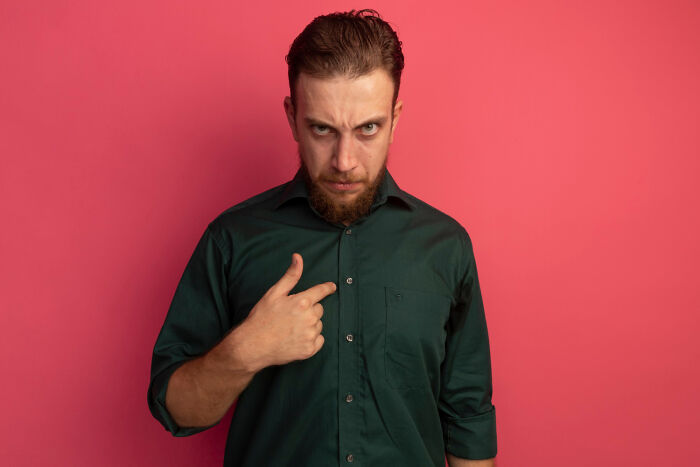 Man in green shirt pointing at himself against a pink background, relating to therapy and parental favoritism.