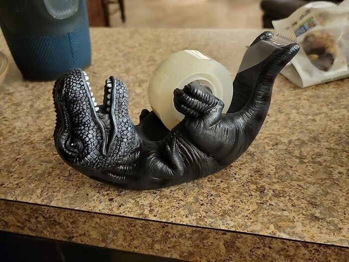 Black dinosaur tape dispenser lying on its back on a kitchen counter, one of the unique Amazon finds.