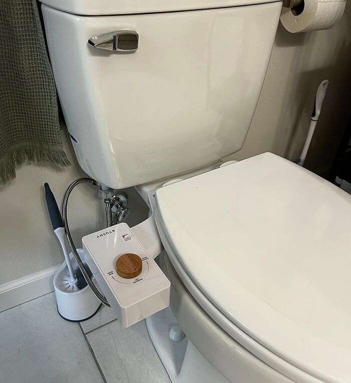 Toilet with a modern bidet attachment and bathroom cleaning tools, showcasing popular bathroom must-haves for convenience and hygiene.