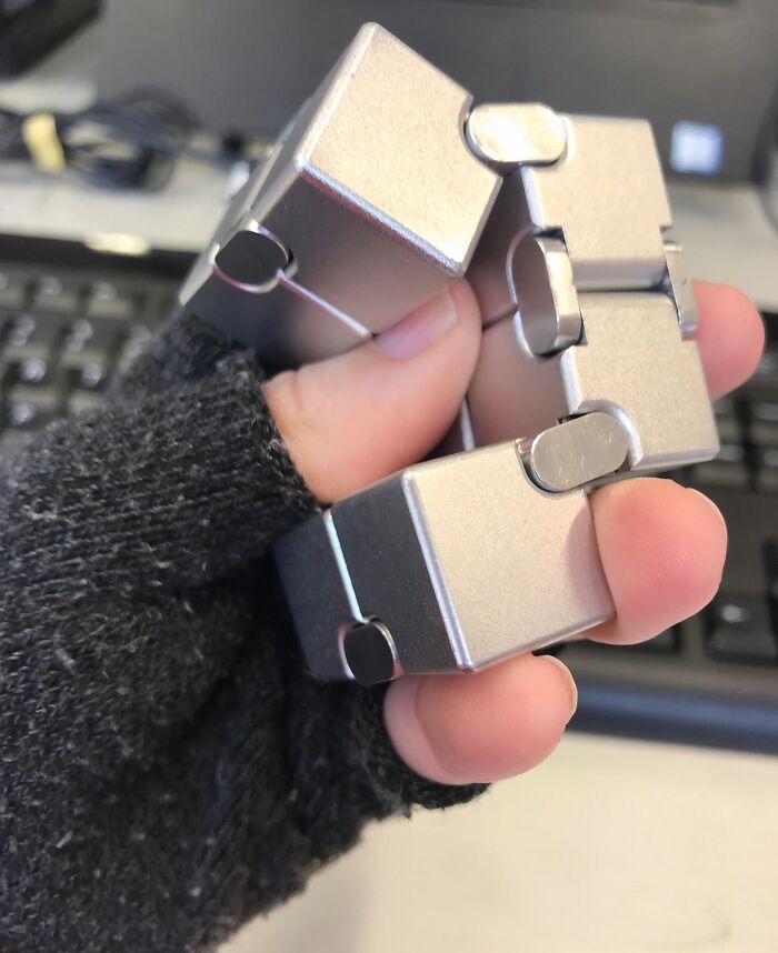 Hand holding a metallic fidget cube toy among Amazon finds that hover delightfully between genius and why does this exist items.
