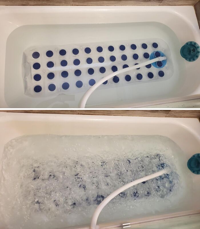 Bathtub with a white non-slip bath mat featuring blue suction cups and a hose creating bubbles in the water.