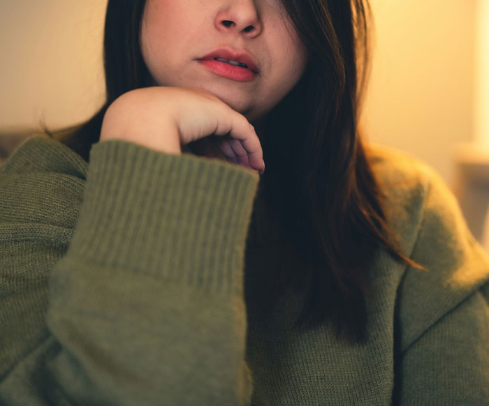 Woman in green sweater, slightly leaning on her hand with lips closed, expressing pensive mood related to cheating revelation.