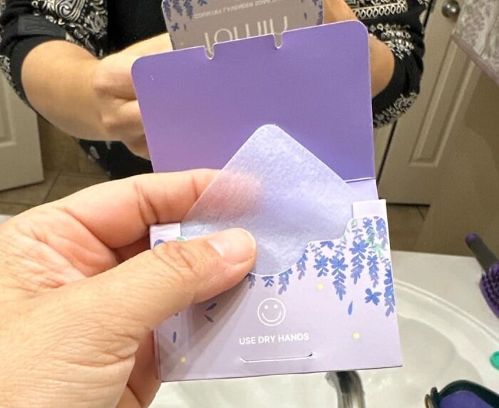 Hand holding lavender sheet from a purple packet in front of a mirror.