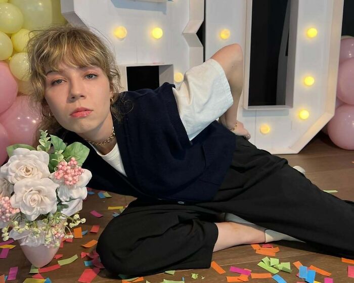 Celebrity striking a pose on the floor amidst colorful confetti and floral decor.