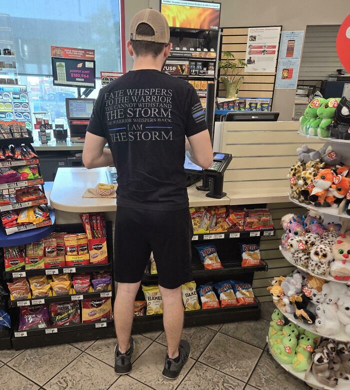 Person in a store wearing a shirt with a dramatic quote, standing by shelves of snacks, embodying cringe behavior.