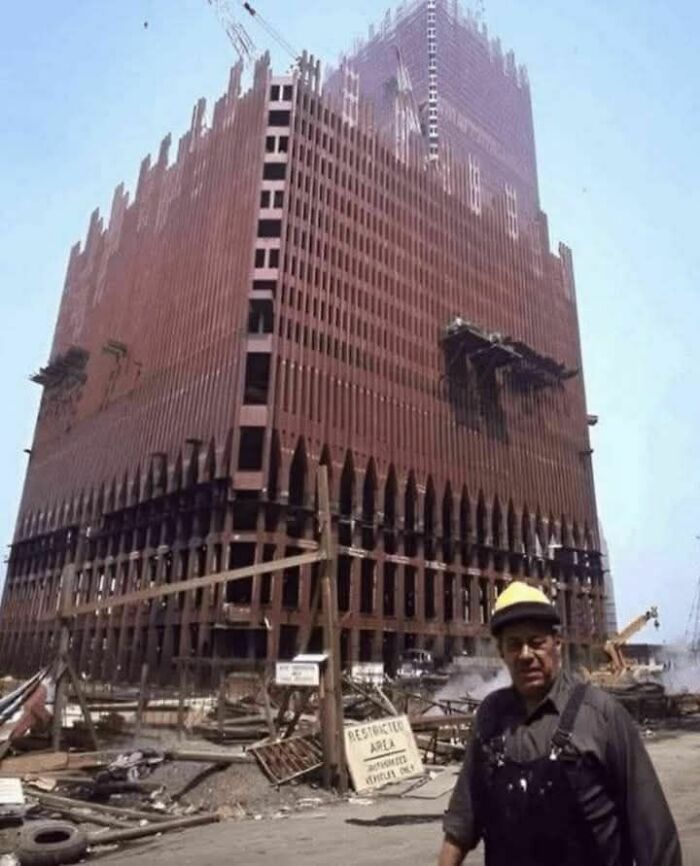 Construction worker stands in front of an unfinished skyscraper, a fascinating old photo for history enthusiasts.