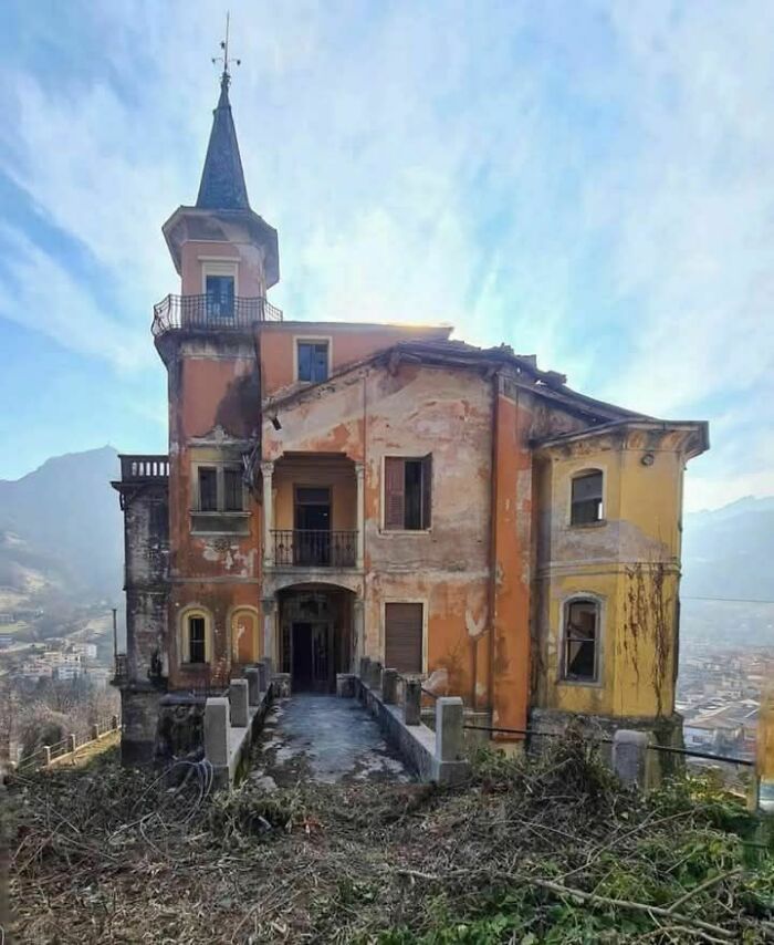 Old photo of an abandoned, weathered house with a tower, set against a mountainous backdrop.