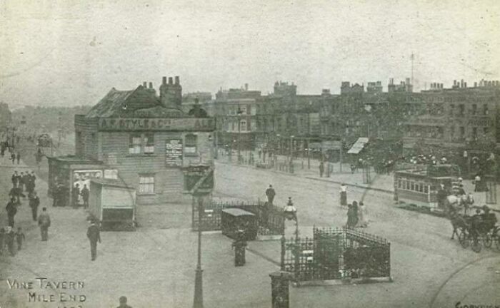 Vintage street scene with Vine Tavern, Mile End, showcasing historical architecture and bustling city life.