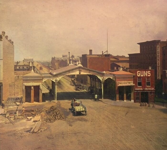 Historical photo showing an old town street with vintage buildings and a cart, capturing a moment in history.