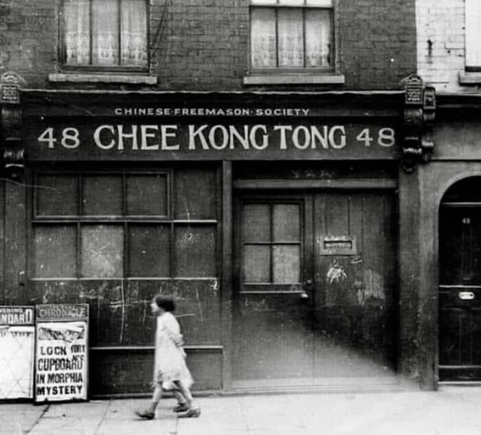 Child walking past historic Chinese Freemason Society building with old sign in black and white photo.