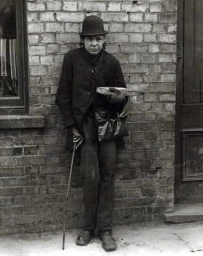 Man in vintage clothing with a cane, standing against a brick wall. Photograph shared by history enthusiasts online.