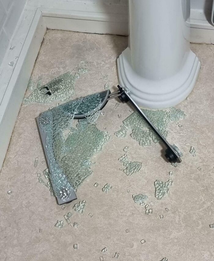 Vidrio templado roto con soporte metálico en el suelo, imagen representando personas con un mal día y accidentes domésticos.