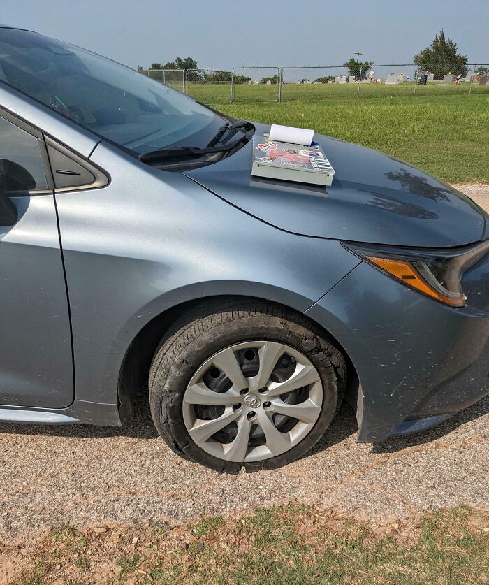 Car with a flat tire parked on a dirt road, showcasing a frustrating day scenario.