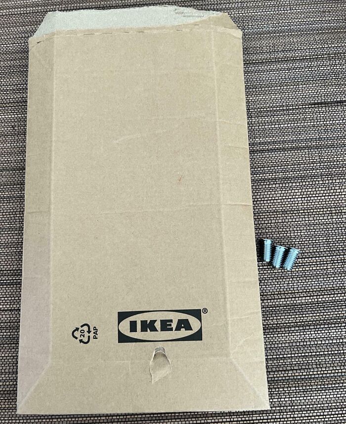 Caja de cartón IKEA con daño visible y varios tornillos junto a ella, imagen de personas que tengan un mal día.