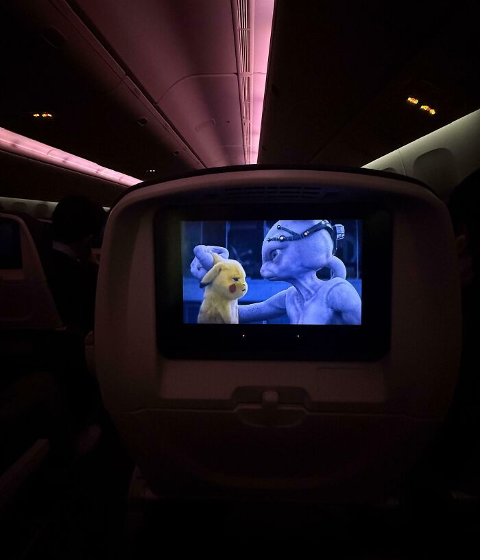 Pantalla en asiento de avión mostrando escena de película con personajes animados, personas que seguramente estén teniendo un mal día.