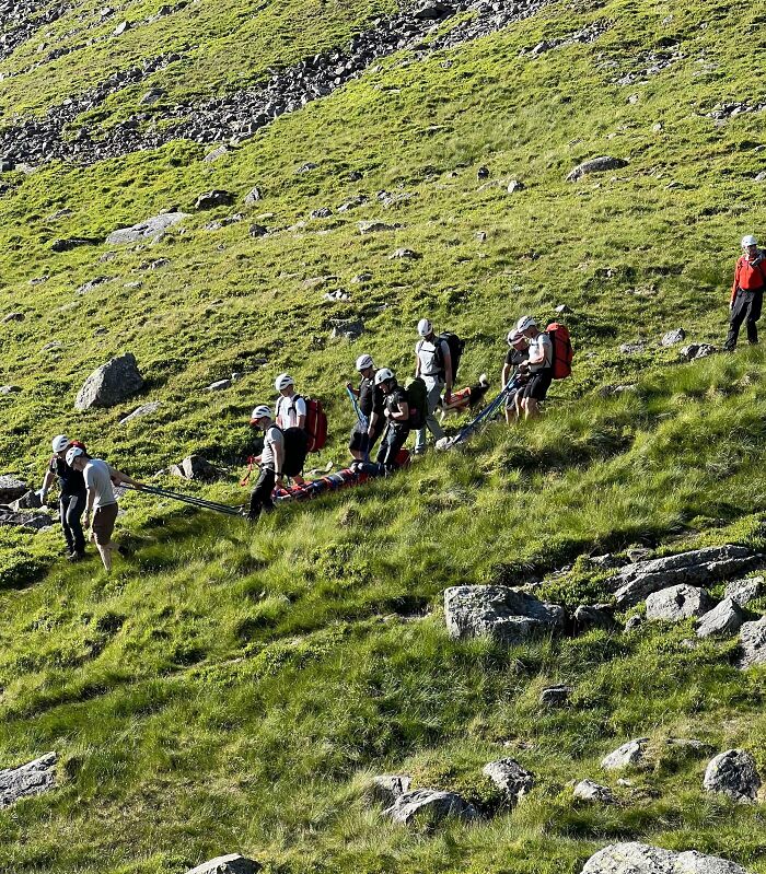 Personas rescatando a alguien en montaña, escena que refleja un mal día en situación de emergencia al aire libre.