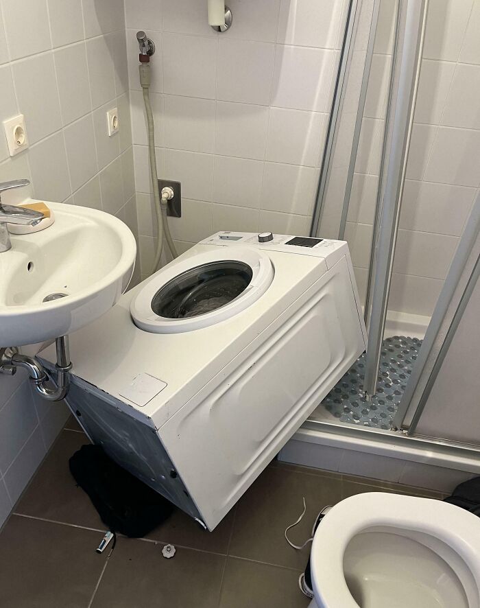 Lavadora caída en baño pequeño junto a lavabo y ducha, ejemplo de personas que seguro estén teniendo un mal día.
