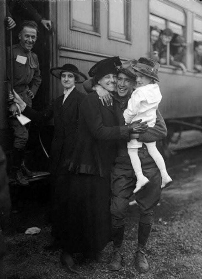 Historic photo of a soldier embracing family at a train station, capturing a poignant moment of reunion.