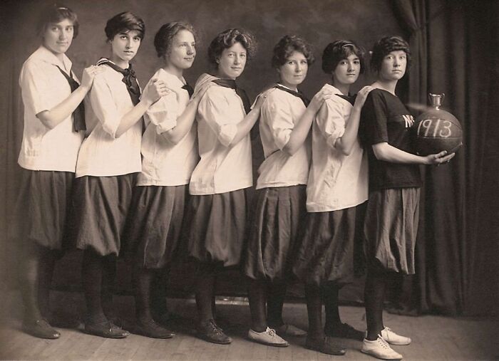 Seven women in vintage attire, lined up holding a 1913 basketball, showcasing old photos shared by history enthusiasts.