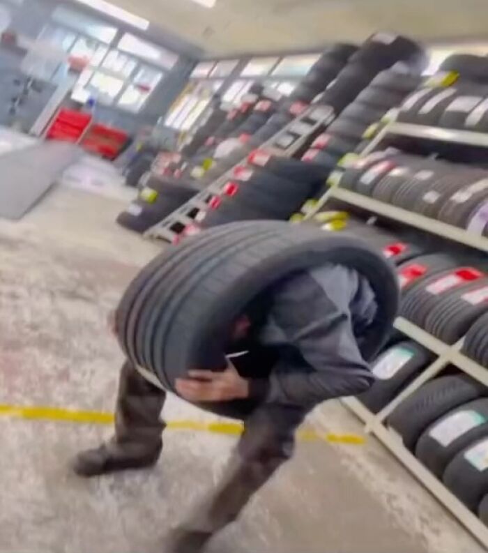 Person humorously stuck inside a tire in a garage, surrounded by stacks of tires, showcasing a funny moment from a popular IG page.