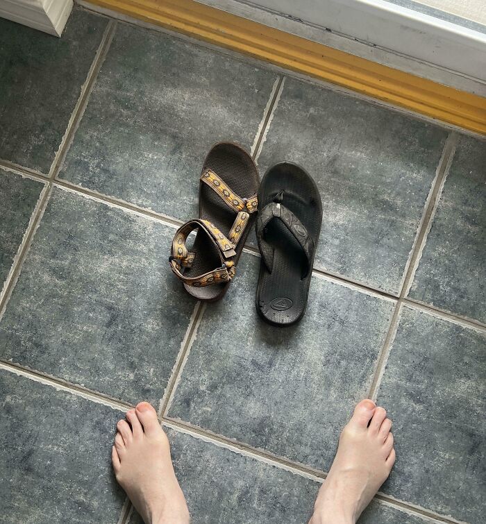 Mismatched sandals on tiled floor next to bare feet, illustrating a humorous mishap.