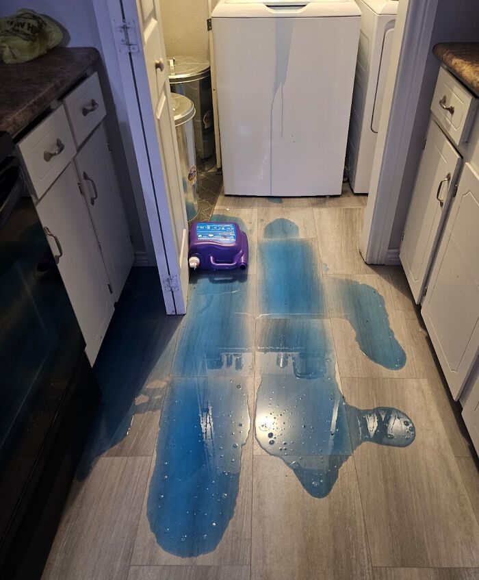 Persona que seguramente esté teniendo un mal día por derramar producto azul en el suelo de la cocina junto a una lavadora.