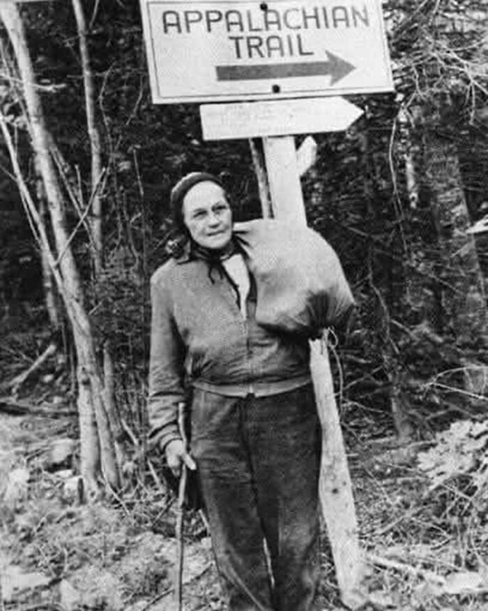 A hiker stands by an Appalachian Trail sign, symbolizing historical hiking adventures.