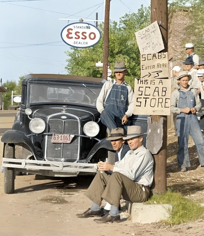 Historic photo of men in overalls near an old car, with signs protesting scabs, outside an Esso station.