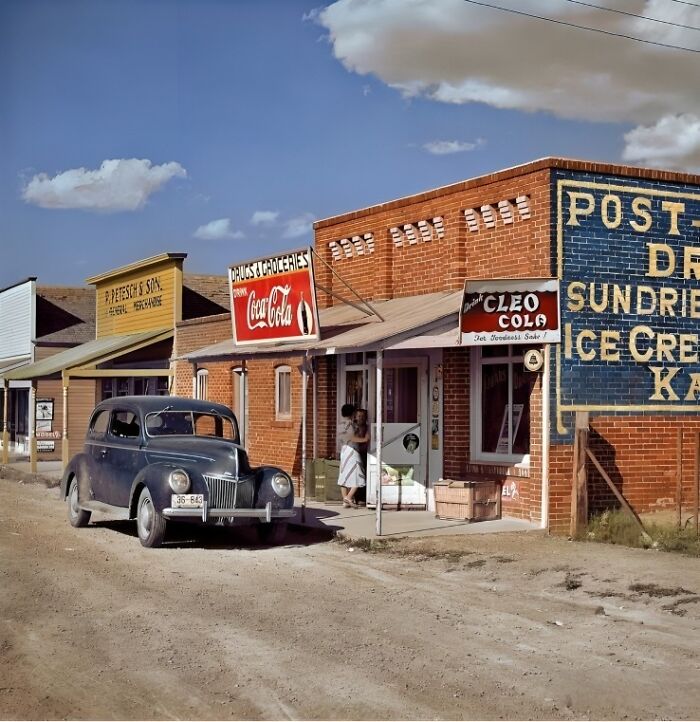 Vintage street scene with an old car parked outside a drugstore and grocery store, showcasing nostalgic historical architecture.
