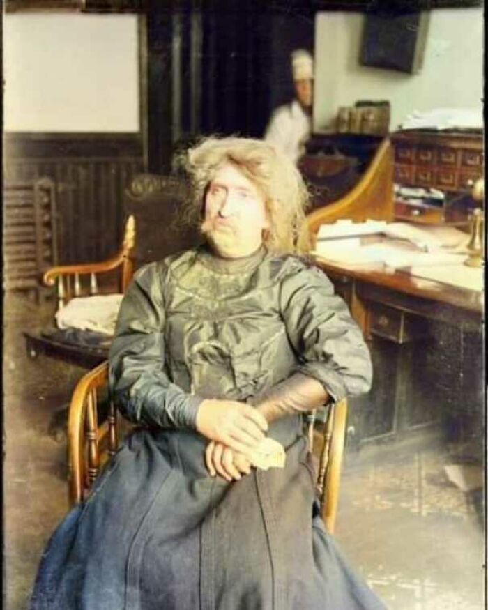 In a historical office setting, a woman seated with hands clasped, showcasing elements of old photos appreciated by enthusiasts.