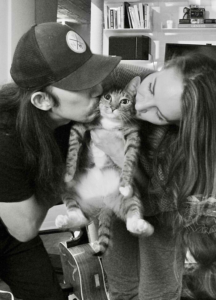 A cat being adored by two people, held gently and kissed on each side, creating a purrfect moment.
