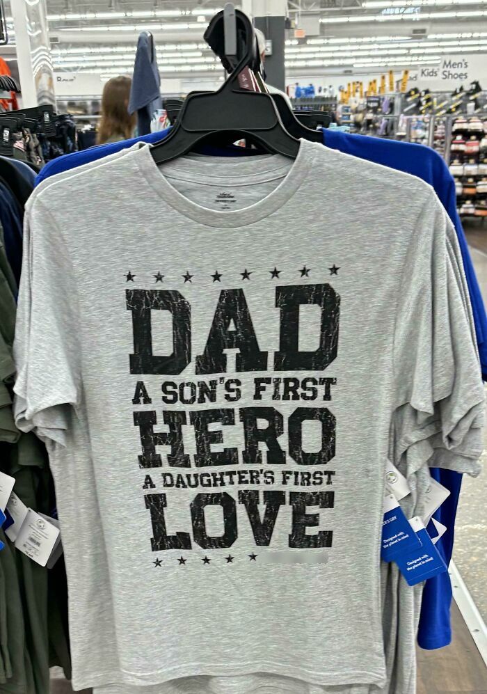 Gray T-shirt with text about dad being a son's first hero and daughter's first love, displayed in a store.