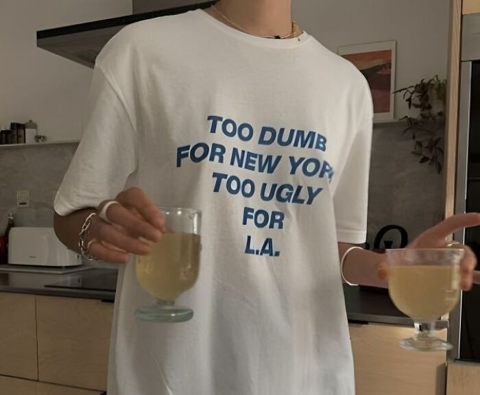 Persona con camiseta divertida blanca con texto en inglés y dos copas con bebida en una cocina moderna.