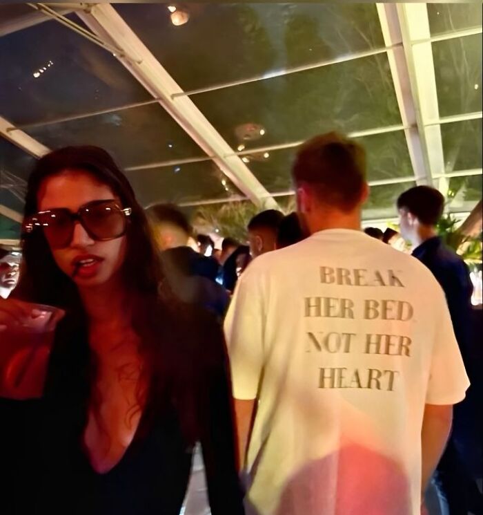 Persona con gafas de sol en fiesta y hombre con camiseta blanca divertida con texto en ambiente social interior.