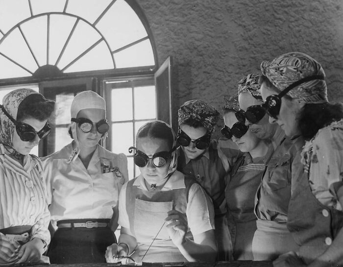Women in protective goggles working together during WWII, focusing on technical details, showcasing a historic moment.
