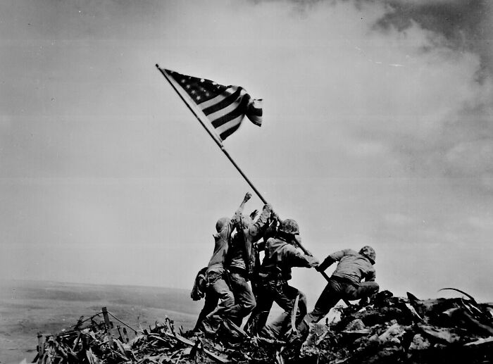 Soldiers raising American flag on Iwo Jima, an iconic WWII photography moment captured against a dramatic sky.