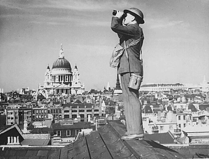 Wartime observer with binoculars on a London rooftop during WWII, protecting the cityscape and St. Paul's Cathedral.