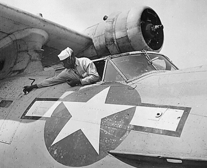 Worker in WWII aviation gear maintains military aircraft, showcasing unforgettable moments in wartime history.