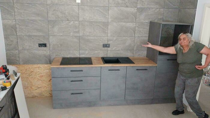 Elderly woman humorously gesturing at a misaligned kitchen counter, highlighting seniors' funny moments.