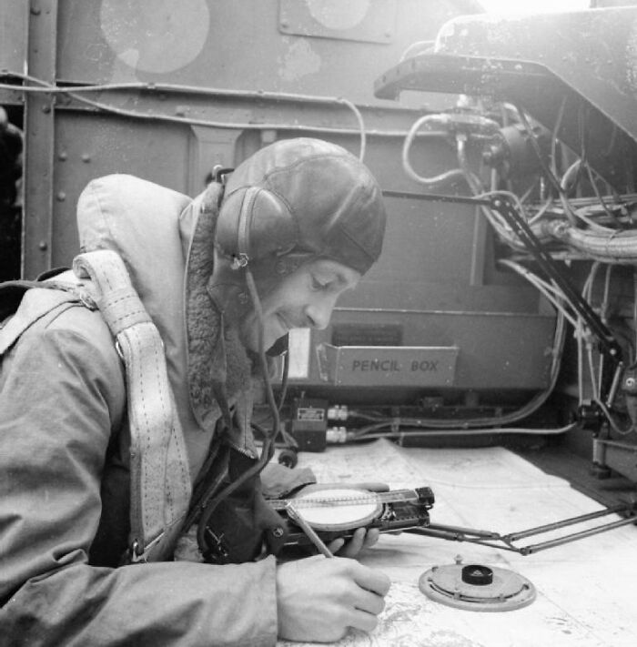 Pilot in WWII gear using navigation tools, a moment captured in historical photography.