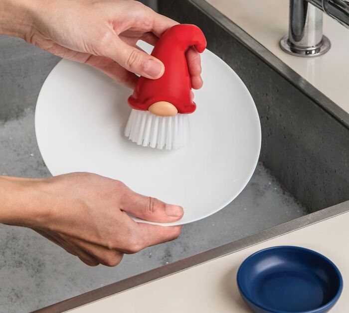 Gnome-shaped scrub brush cleaning a dish in a sink.