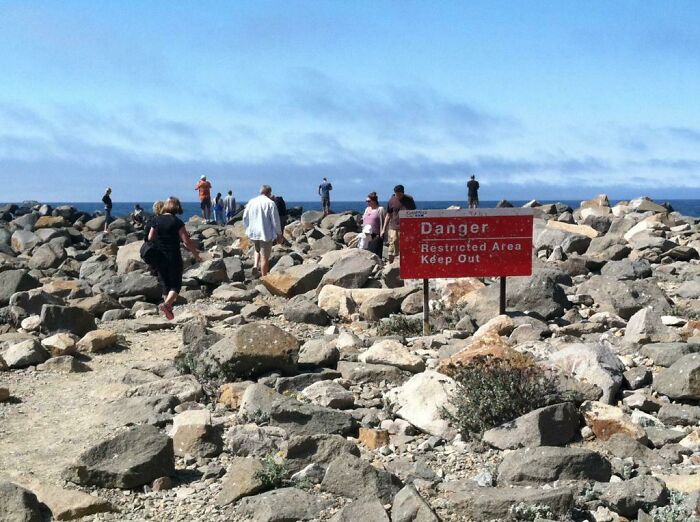 People walking on rocky terrain past a danger sign, highlighting something dangerous.